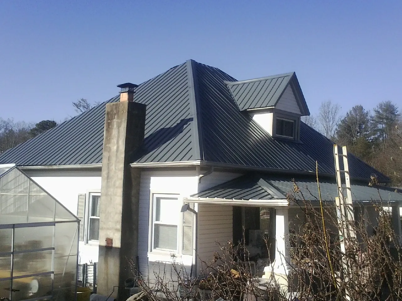 Dark blue standing seam metal roof on a white farmhouse with dormer — Slate & Tile Roof Repair by Roofing Brothers in Max