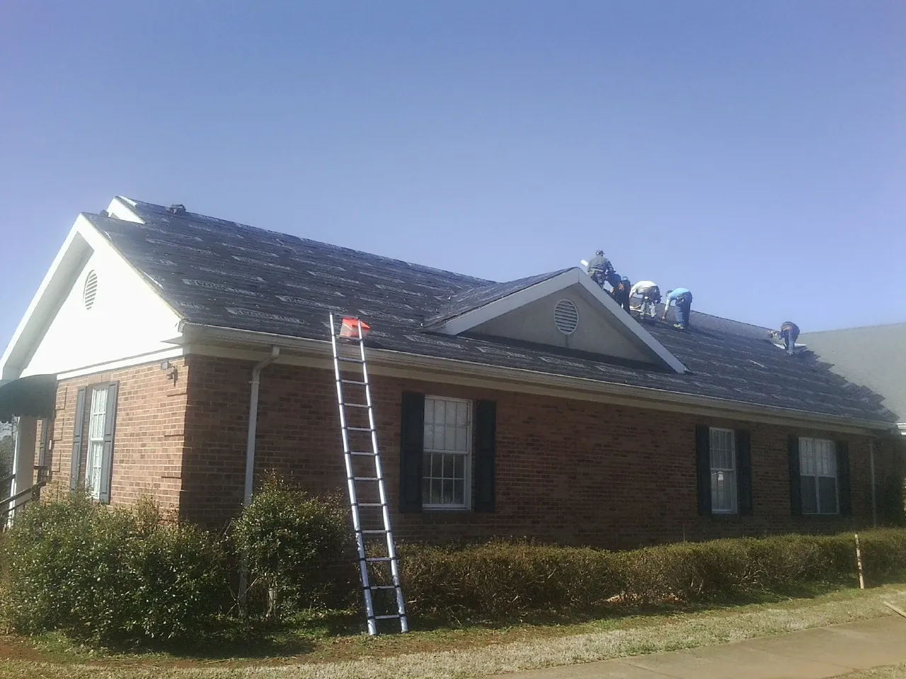Crew tearing shingles off a brick ranch roof with a ladder set — Metal Roof Repair work by our crew in Max