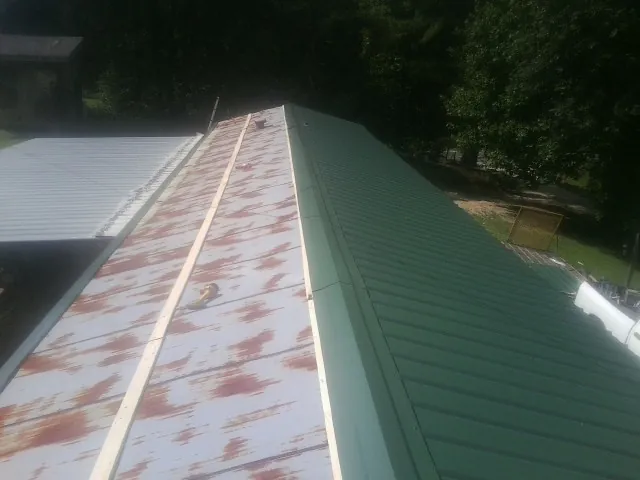 Old rusted panels beside newly installed green metal roofing — Wind Damage Roof Repair by Roofing Brothers in Max