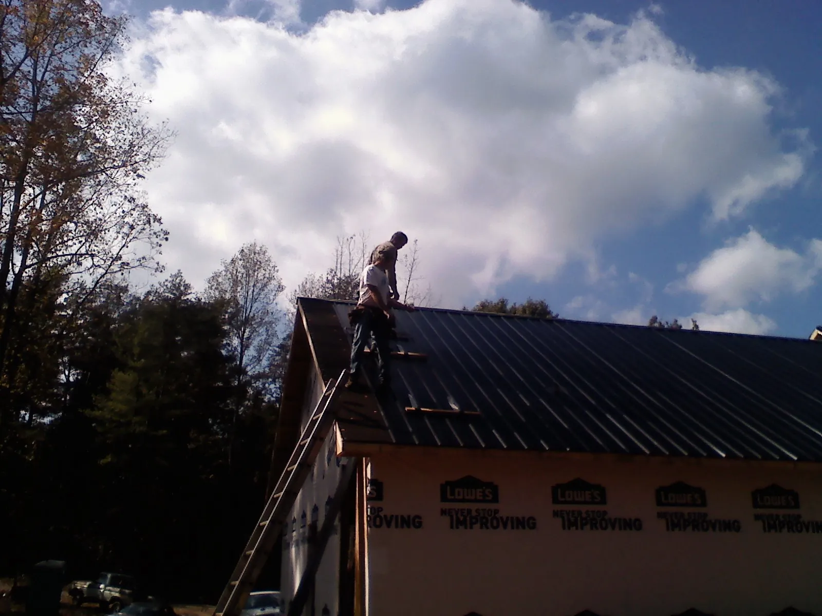 Roofer fastening dark metal panels high against a cloudy sky, from a Roof Inspection job in Max