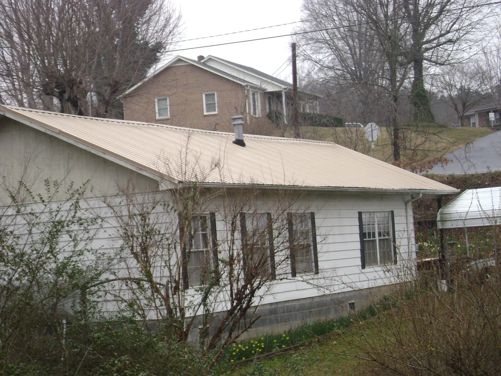 Tan metal roof on a white sided house set into a hillside — Commercial Roofing by Roofing Brothers in Max