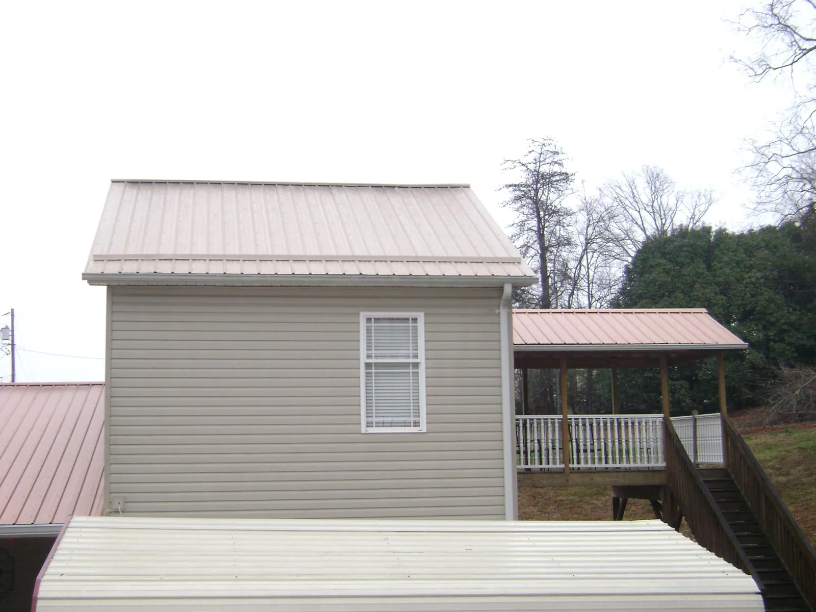 Tan metal roofs on a two story addition and attached porch, from a Roof Replacement job in Max